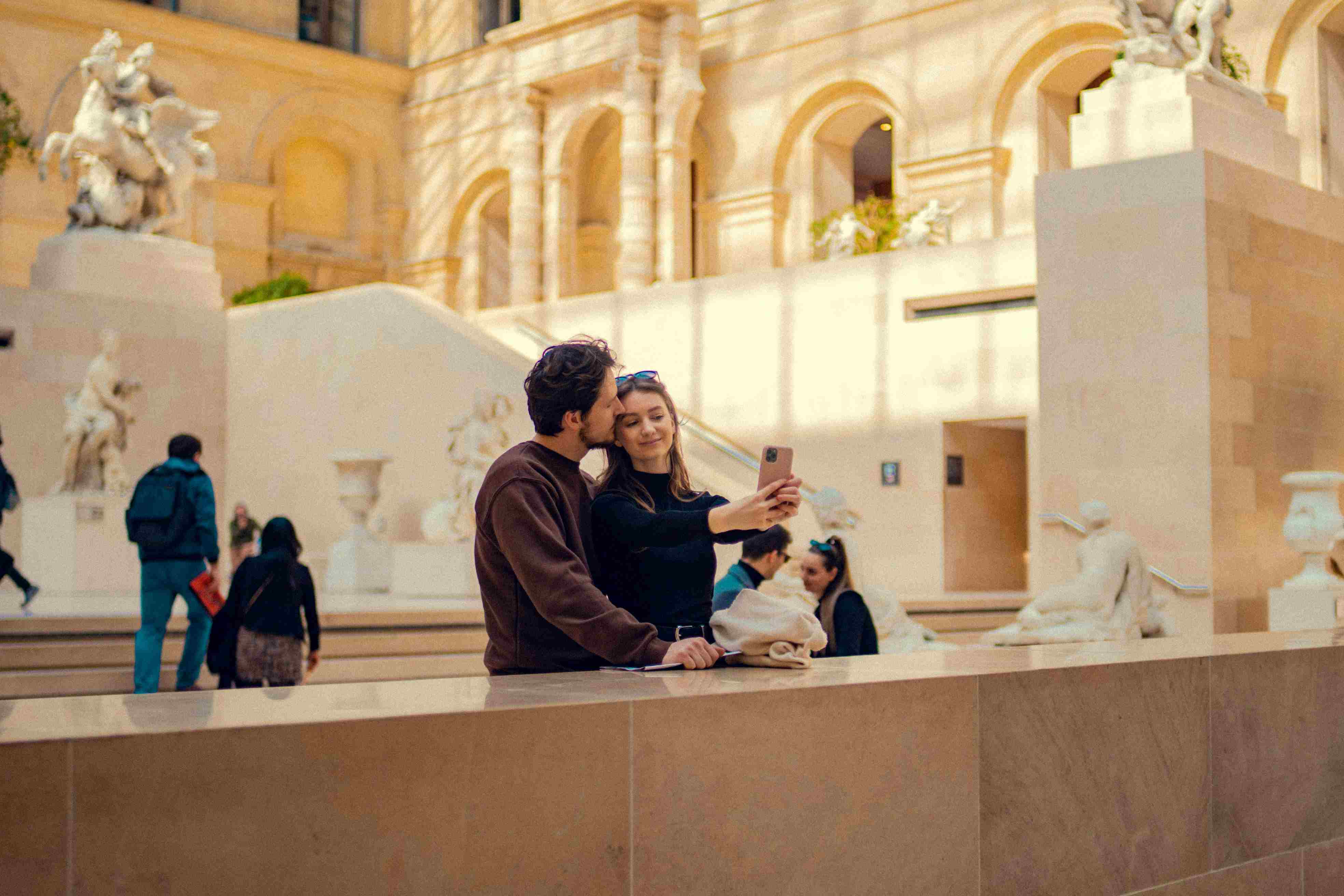 A couple taking a picture on their honeymoon at a large marble staircase in the Louvre